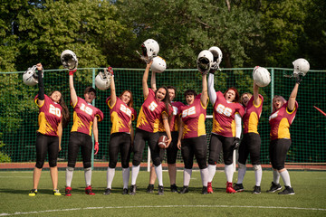 Full length photo of female rugby team with raised hands looking at camera