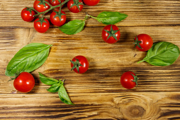 Fresh cherry tomatoes with green basil leaves on a wooden table. Top view