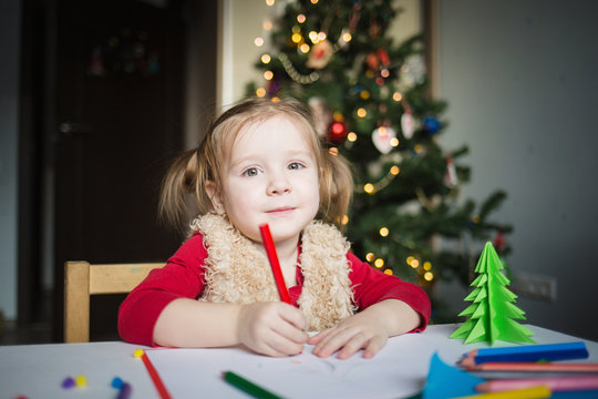 the child writes a letter to Santa Claus. a little girl draws with crayons on the background of the Christmas tree. the concept of new year kids creativity