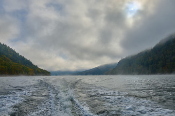 The trail of the boat (Wake) on a Norwegian lake in the middle of the mountains and fog in the autumn. Boat trip on the lake in autumn