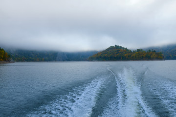 The trail of the boat (Wake) on the lake in the middle of the mountains and fog in the autumn. Boat trip on the lake in autumn in Alaska