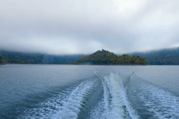 The trail of the boat (Wake) on the lake in the middle of the mountains and fog in the autumn. Boat trip on the lake in autumn in Alaska