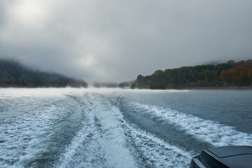 Walk on a mountain lake on a boat in the fog in the autumn. Boat fog fall. The trace of the boat on the water (Wake)