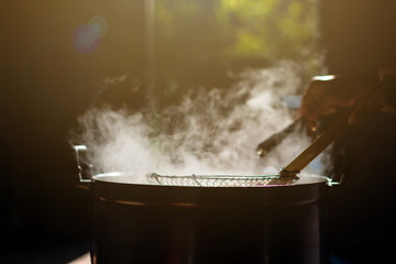 Cooking person in the restaurant is cooking while using the dipper in a large pot. And the water is boiling, there is smoke, hot spit.