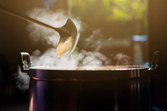 Cooking Person In The Restaurant Is Cooking While Using The Dipper In A Large Pot. And The Water Is Boiling, There Is Smoke, Hot Spit.