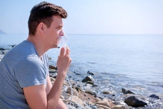 Portrait Sick Man Uses Nebulizer Sits On Seaside. Inhaling Inhaler Mask. Fibrosis Cystic Copd And Treatment Inhaler. Asthma Pulmonary Respiratory Breath Problem Cure. Painkiller Sedative Gas Oxygen.