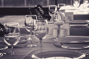 Table setting in restaurant. Empty wine glasses, plates, forks, knifes on the tablecloth. Elegant restaurant interior.