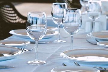 Table setting in restaurant. Empty wine glasses, plates, forks, knifes on the tablecloth. Elegant restaurant interior.