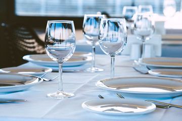 Table setting in restaurant. Empty wine glasses, plates, forks, knifes on the tablecloth. Elegant restaurant interior.