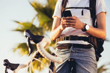 Young handsome guy equipped cyclist smiles and chats with his girlfriend using a smartphone on a sunny summer day while relaxing from a trip. Vacation activities concept