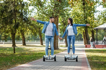 Fototapeta premium A young couple riding a hoverboard in a park, self-balancing scooter. Active lifestyle technology future