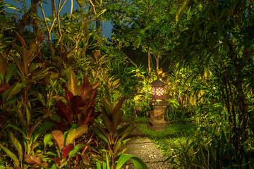 Decorative lamp on the stone pillar next to the path in the tropical garden at night . Island Bali, Indonesia . Nature concept