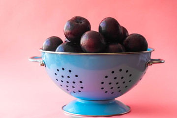 bunch of ripe plums in blue metal bowl on pink background