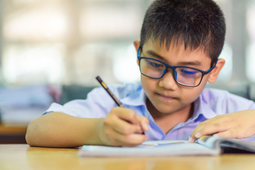 Asian elementary school boy in a white school uniform and wearing glasses, is studying in the...