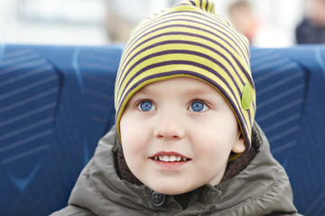 Little beautiful caucasian baby boy with bright blue eyes smiling, outdoors. Casual autumn, spring wear, yellow striped hat. Copy space.