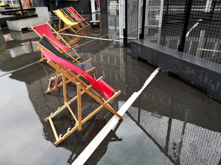 Liegestühle in Rot auf nassem spiegelnden Asphalt mit Bierkiste als Beistelltisch bei Regenwetter...