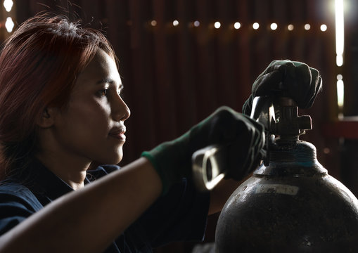 Mechanical engineer woman using wrench hand tool to repair valve on gas cylinder - Diverse Asian female mechanic working in industrial workshop with oxygen tank - service, fix and equality concept