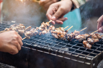 People standing toast, grilled chicken and pork on the stove with smoke in the celebration.