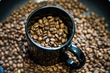 Roasted brown coffee grains in a black cup