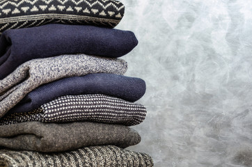 Stack of folded warm knitted men's sweaters on gray background. Closeup. Copy space