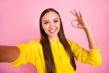 Self portrait of cheerful cute pretty sweet lovely fascinating girlfriend brunette haired showing you ok sign taking selfie wearing yellow sweater while isolated over pink pastel color background