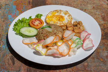 Fried rice with vegetables, rice chips, cheese tofu and fried egg on the old wooden table in local cafe, close up indonesian cuisine. Breakfast in Bali, Indonesia