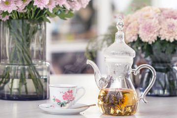 Teapot and cup with blooming tea flower and pink Chrysanthemum flowers in glass vase on table.