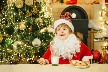 Cheerful Santa Claus holding glass with milk and cookie with fireplace and Christmas Tree in the background. Christmas cookies and milk.