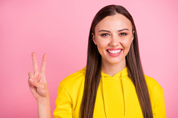 Close up photo of funny cheerful cute nice gorgeous youngster girlfriend smiling toothily cheerfully showing you v-sign while wearing yellow sweater isolated with pink pastel color background