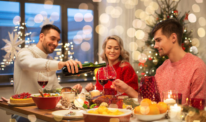 holidays and celebration concept - happy friends having christmas dinner at home and drinking red wine