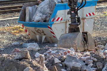 Mobilbagger mit Zweischalengreifer sorgt für Ordnung auf der Baustelle und beseitigt Schutt und Geröll durch viel PS neben Bahngleisen für Gleisarbeiten mit Schuttcontainer