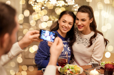 holidays and celebration concept - happy friends having christmas dinner at home and taking picture by smartphone