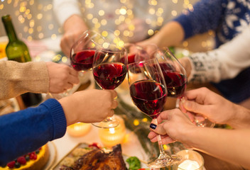 holidays and celebration concept - close up of friends having christmas dinner at home, drinking red wine and clinking glasses