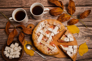 Autumn composition. Homemade Apple pie, autumn leaves, two mugs of tea, sugar cubes on a wooden background.
