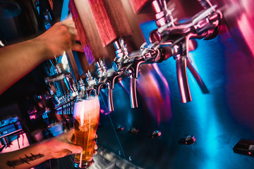 Hand of bartender pouring a large lager beer in tap. Bright and modern neon light, males hands....