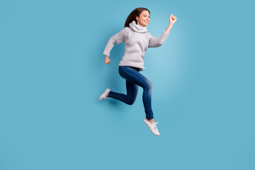 Fototapeta na wymiar Full length profile side photo of glad charming girl jump run hurry after bargain feel content have free time wear white knitted sweater pullover jeans sneakers isolated over blue color background