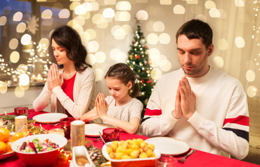 holidays, family and celebration concept - happy mother, father and little daughter having christmas dinner and praying before meal at home