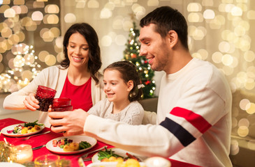 holidays, family and celebration concept - happy mother, father and little daughter having christmas dinner at home