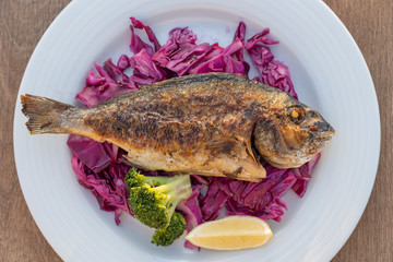 Grilled sea fish served on a plate with red cabbage, green broccoli and lemon. Close up