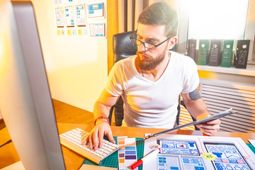 A man with a beard works as a mobile app designer. The designer tests the created layout of the user interface of the program. Development of graphic and color solutions for mobile applications.