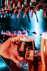 Hand of bartender pouring a large ale, porter, stout beer in tap. Bright and modern neon light, males hands. Pouring beer for client. Side view of young bartender pouring beer while standing at the