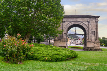 Obraz premium View of the Arch of Augustus, a monument erected in 25 BC on the occasion of the Roman victory over the Salassi, from a public park in summer, Aosta, Aosta Valley, Italy