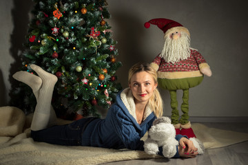 young woman lies near a Christmas tree with soft toy