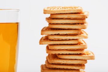 A stack of golden wheat cookies and a mug of fragrant green tea in on a white background. Cookies laid out in a breakfast column and a golden highlight with tea mugs