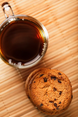 Oatmeal cookies with pieces of chocolate and a mug of coffee on a bamboo stand. Close-up
