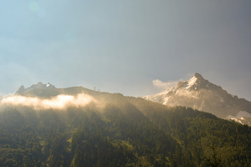 Scenic view of the mountain tops of Plan Checrouit (1709 m) and the snowcapped Pointe Helbronner (3462 m) peak of the Mont Blanc massif in the background, with lens flare, Courmayeur, Aosta, Italy