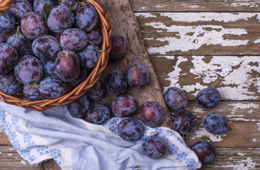 Purple plums in a basket on a wooden table.