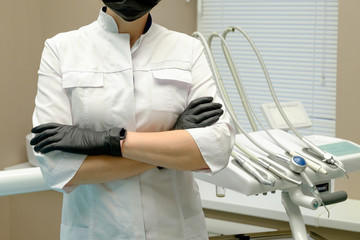 Girl dentist stands arms crossed on the background of the dental unit