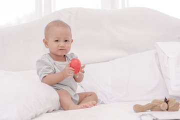 Little cute baby one year girl sitting and playing alone on white bed.