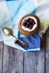 Berry dessert with yogurt in a cup of coconut on a wooden background. Blackberries, raspberries, blueberries, black currants. Blue napkin
